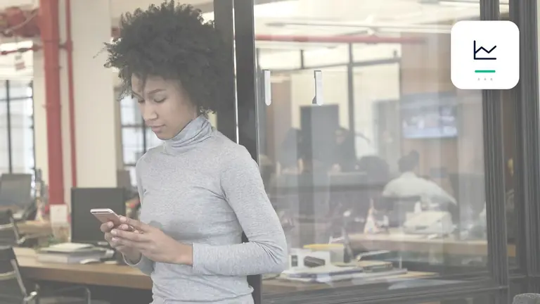 Mitarbeiterin mit Smartphone in einem transparenten modernen Büro mit klarer Kennzahlen-Grafik – Symbolbild zum Beitrag „Forderungsmanagement 2026: Die wichtigsten Trends zwischen Digitalisierung und Ausfallrisiko“.