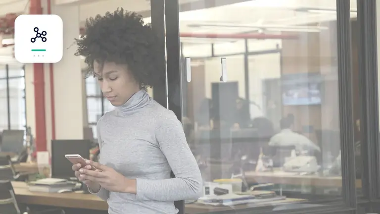 Mitarbeiterin mit Smartphone in einem transparenten modernen Büro mit digitalem Prozessnetzwerk – Symbolbild zum Beitrag „Forderungsmanagement automatisieren: Welche Aufgaben sich wirklich eignen“.