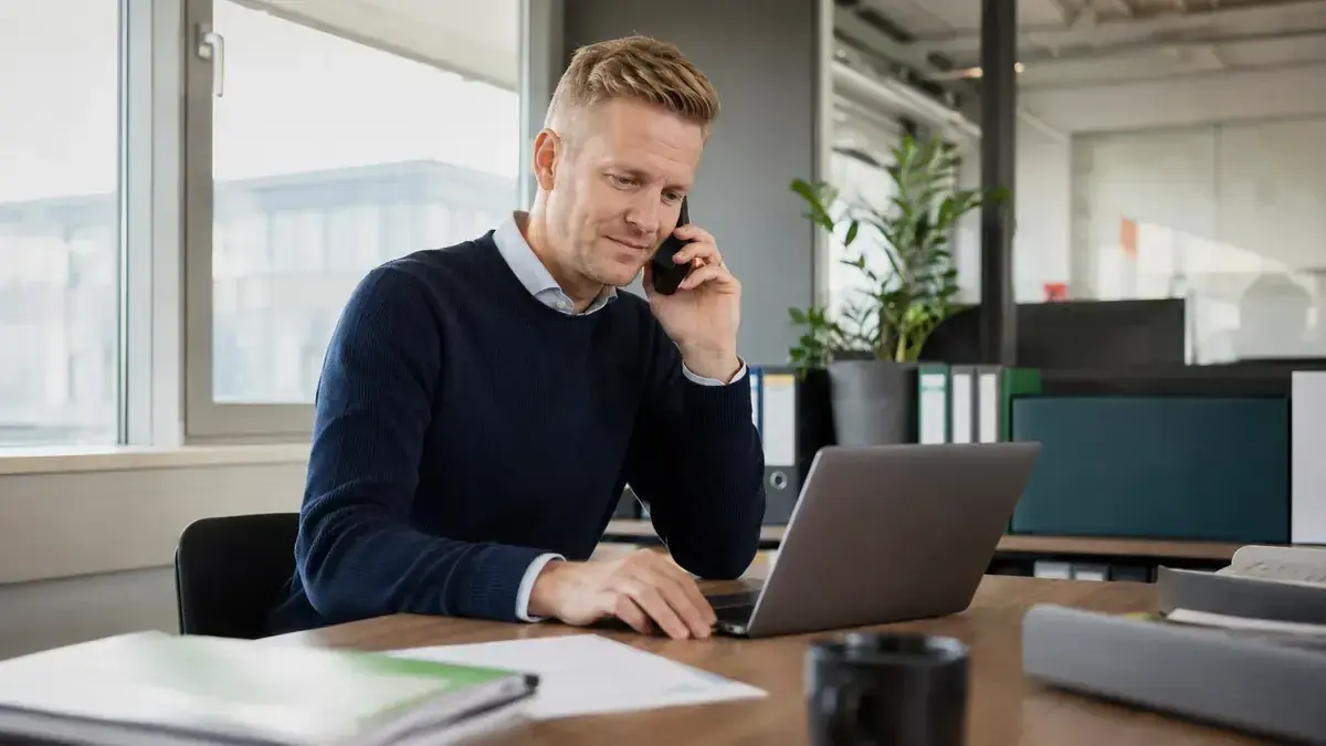 Mitarbeiter im modernen Büro mit Laptop und Telefon mit persönlicher Geschäftskommunikation – Symbolbild zum Beitrag „Forderungsmanagement kundenfreundlich gestalten: Konsequenz ohne unnötige Härte“.