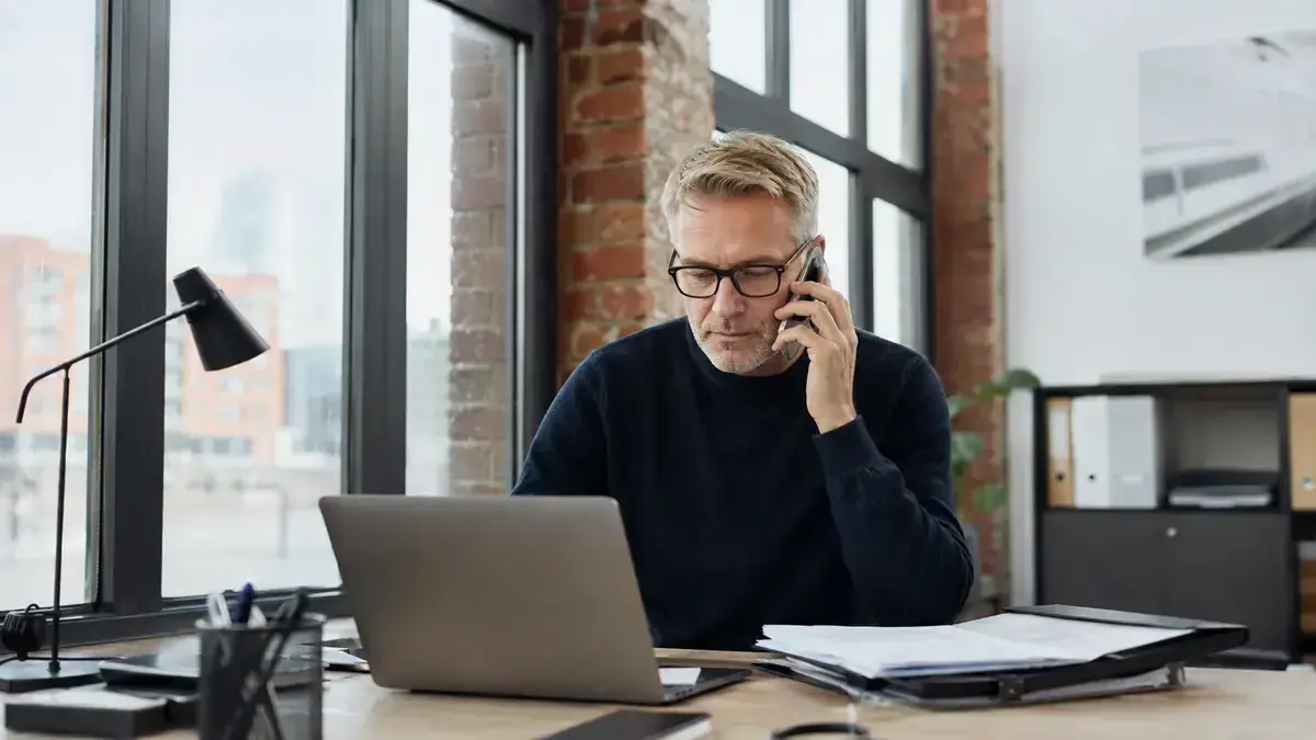 Mitarbeiter im modernen Büro mit Laptop und Telefon mit digitalem Rechnungsdokument – Symbolbild zum Beitrag „Inkasso für Agenturen und Freelancer: Honorare strukturiert einfordern“.