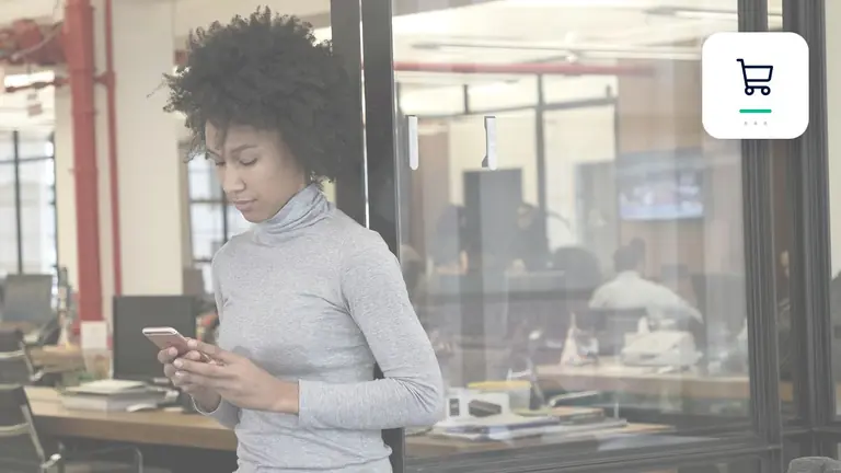 Profesional con un teléfono móvil en una oficina moderna y diáfana con símbolo de comercio electrónico y pago – imagen editorial para «Cobro de deudas para tiendas online: qué cuenta en entregas, devoluciones y…