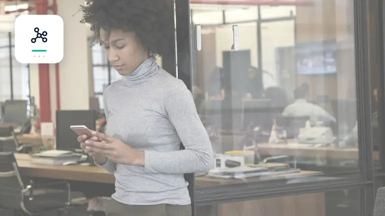 Profesional con un teléfono móvil en una oficina moderna y diáfana con red digital de procesos – imagen editorial para «Cobro de deudas con IA: obligaciones de transparencia para chatbots y comunicación automatizada».