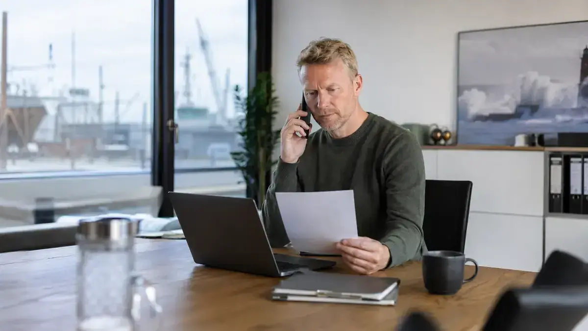 Mitarbeiter im modernen Büro mit Laptop und Telefon mit digitalem Rechnungsdokument – Symbolbild zum Beitrag „Rechnung wird nicht bezahlt bei Agentur- oder Freelance-Arbeit: Leistungsnachweise nutzen“.
